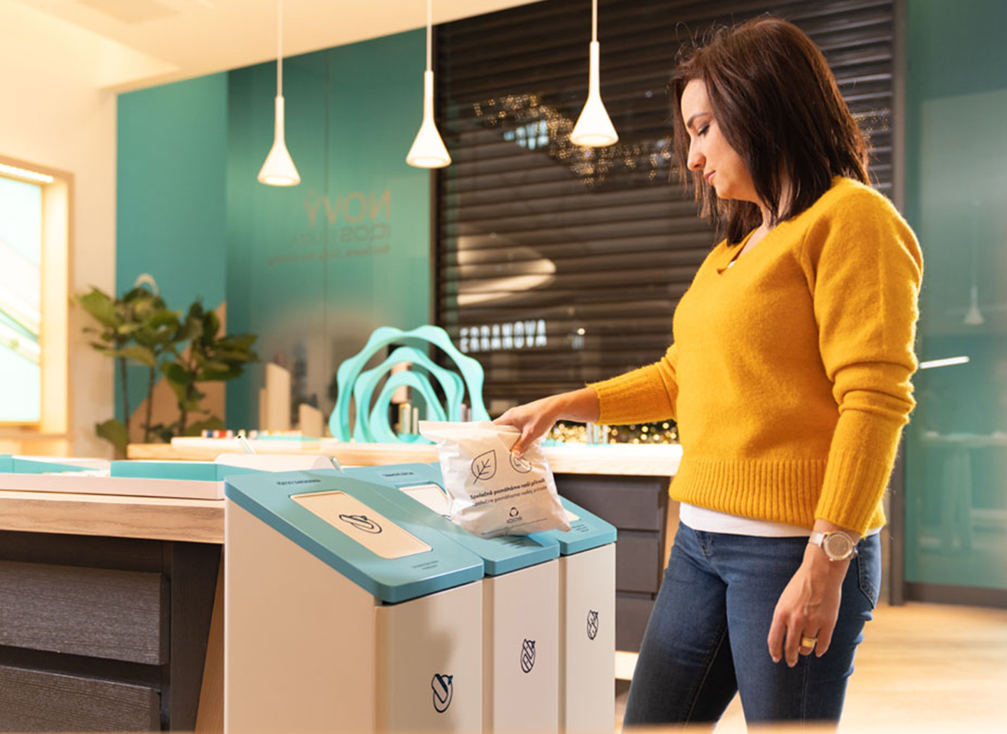 A woman throws a full collection bag of consumables into a collection bin.