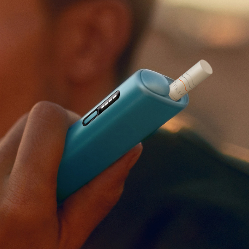 Deatail of hand holding a blue IQOS ILUMA i ONE device