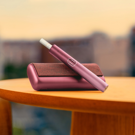 Garnet Red IQOS ILUMA i PRIME device above its charger, on a table