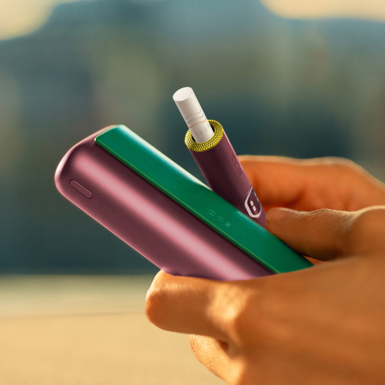 Hand holding an IQOS ILUMA i PRIME device and its charger customed with a wrap