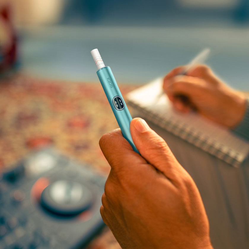 Hand holding a blue IQOS ILUMA i device, while writing notes