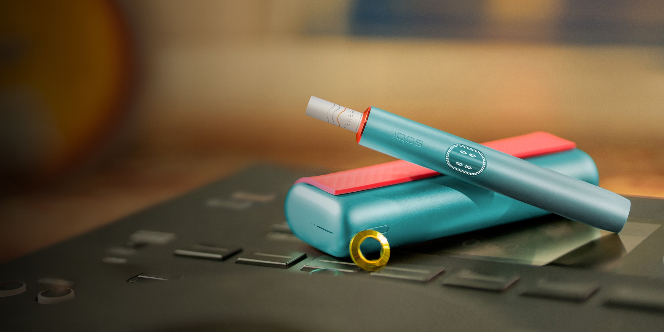 Blue IQOS ILUMA i PRIME device above its charger, customized with wrap and rings