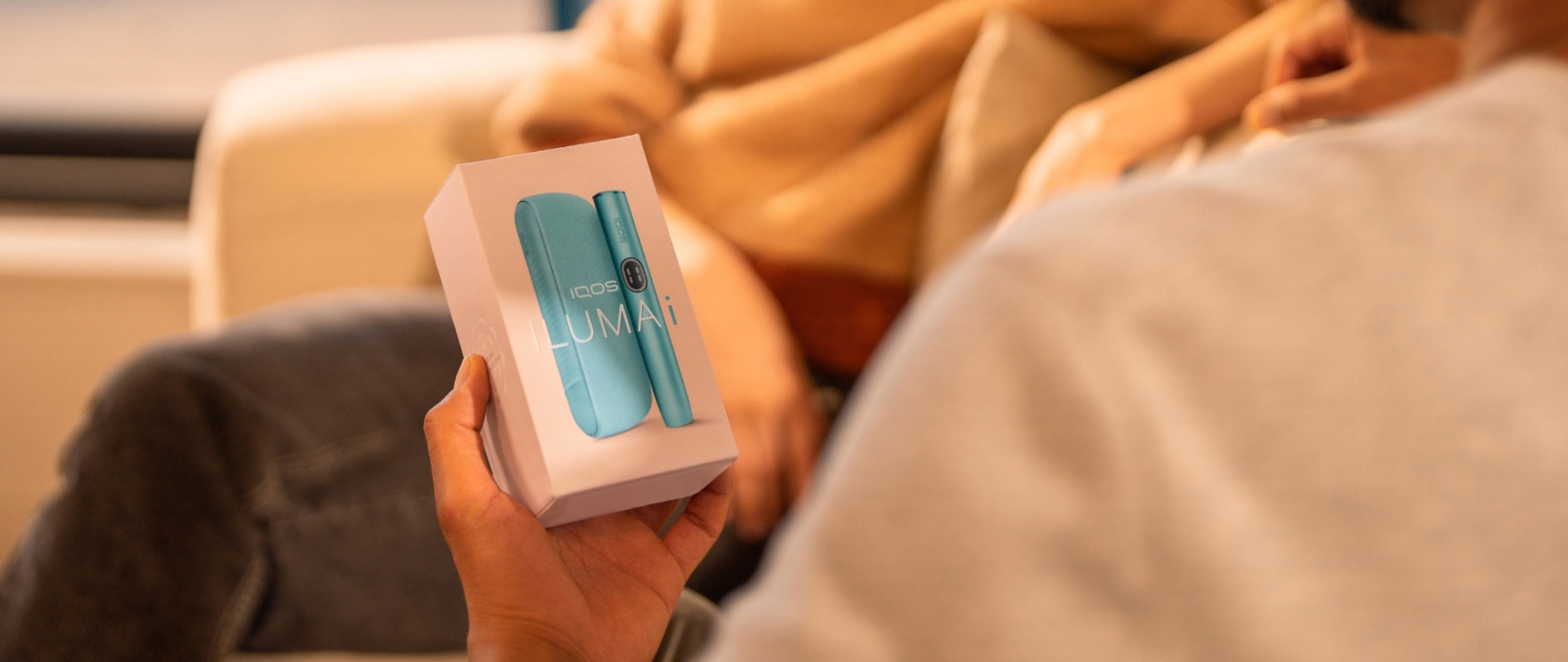 Person holding an IQOS device package featuring a turquoise IQOS ILUMA device and holder.