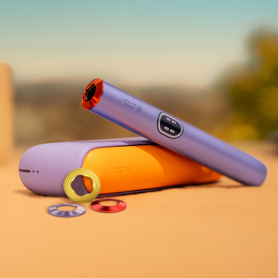 Appareil IQOS ILUMA i (stylet + chargeur) couleur Lila personnalisé avec un clip orange sur le chargeur de poche et une bague rouge sur le stylet. A côté de l'appareil, sont disposés 3 bagues de personnalisation IQOS ILUMA i de couleurs différentes : lila, jaune et rouge.