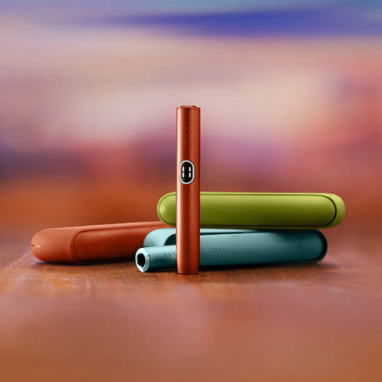 Vue de face d'un stylet IQOS ILUMA i couleur Terracotta avec en arrière-plan trois chargeurs de poches IQOS ILUMA i, un couleur Vert Anis, un couleur Terracotta et un couleur Aigue-Marine