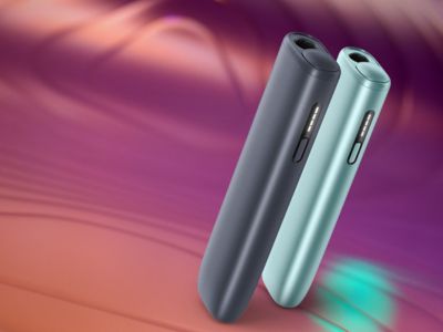 Deux appareils IQOS ILUMA i ONE (appareil tout-en-un) couleurs Noir Intense et Aigue-Marine, posés , sur un fond violet.