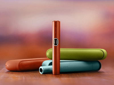 Vue de face d'un stylet IQOS ILUMA i couleur Terracotta avec en arrière-plan trois chargeurs de poches IQOS ILUMA i, un couleur Vert Anis, un couleur Terracotta et un couleur Aigue-Marine