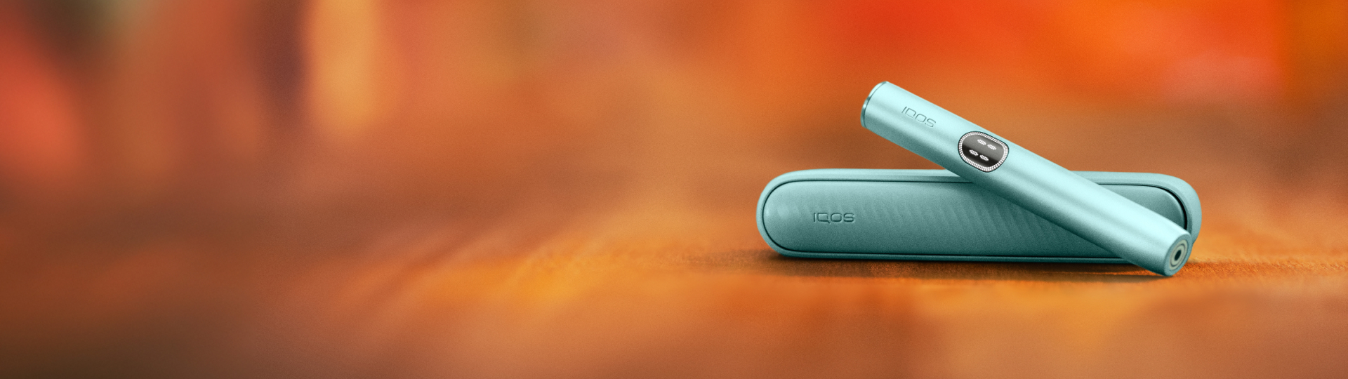 Appareil IQOS ILUMA i couleur Aigue-Marine posé sur un fond dégradé orange.
