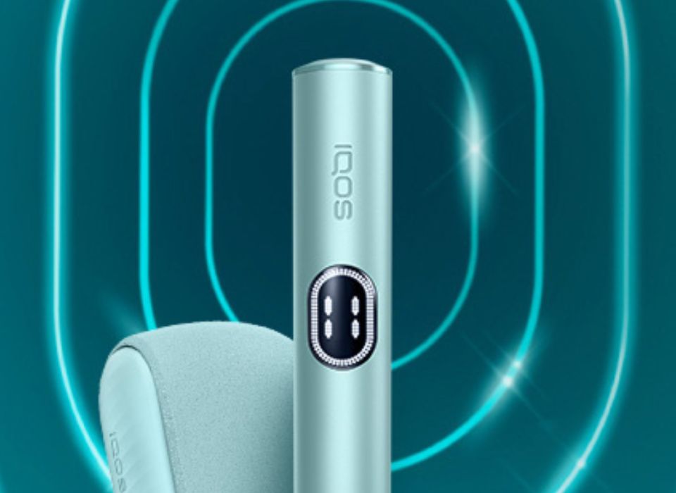 Kit IQOS ILUMA i (stylet + chargeur) couleur Aigue-Marine, sur un fond dégradé bleu.