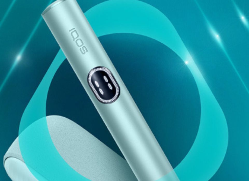Kit IQOS ILUMA i (stylet + chargeur) couleur Aigue-Marine, sur un fond dégradé bleu, avec par-dessus, le logo de la quille IQOS.