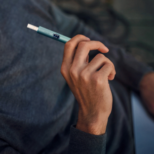 A man working on a laptop while holding an IQOS ILUMA device.