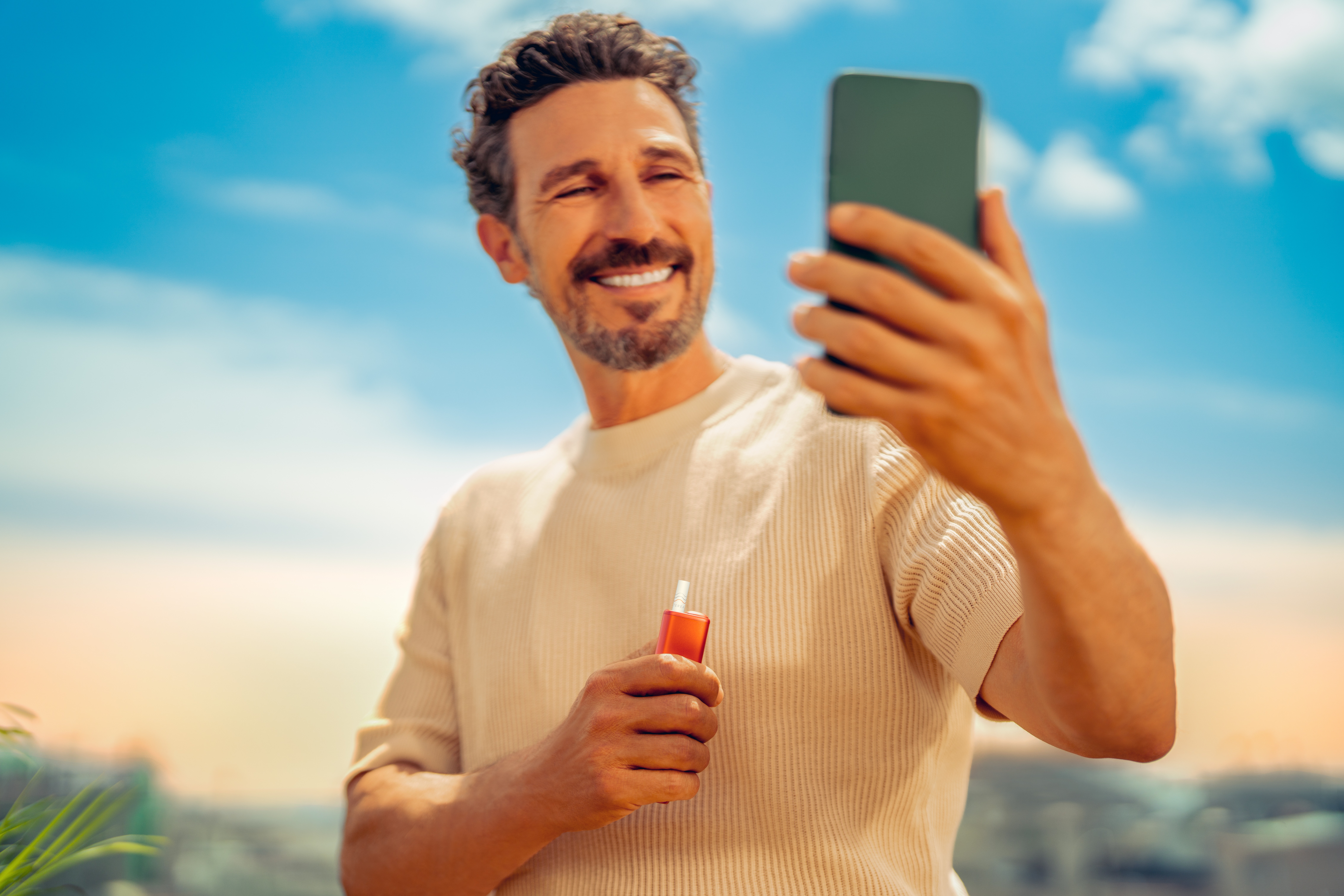 Hands typing on laptop and Iphone next to turquoise IQOS ORIGINALS DUO pocket charger.