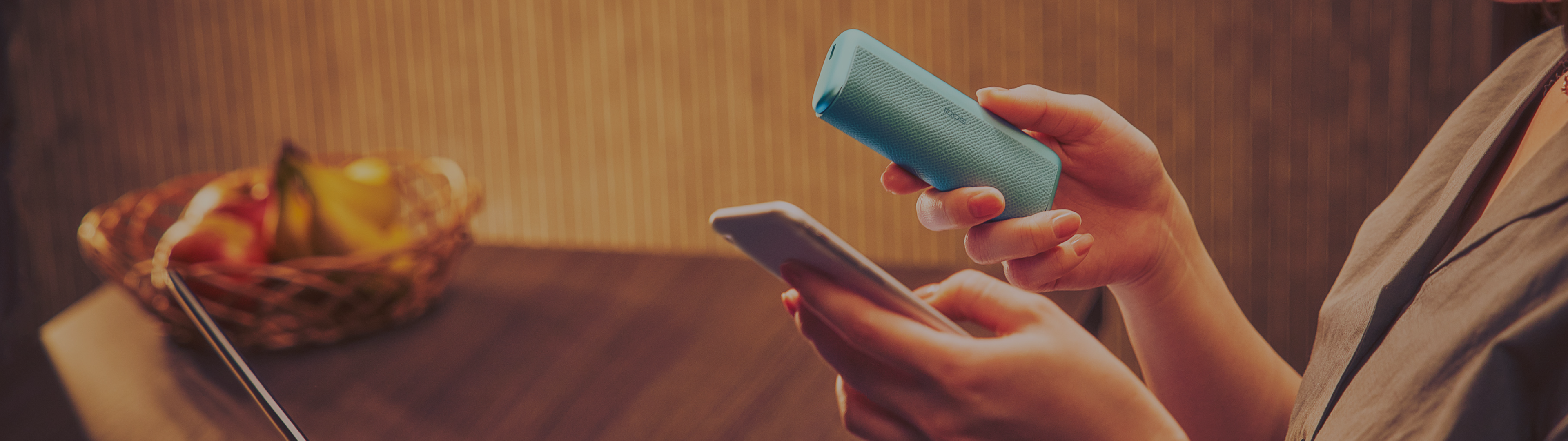 Person hält ein IQOS ILUMA i PRIME und ein Smartphone in den Händen.