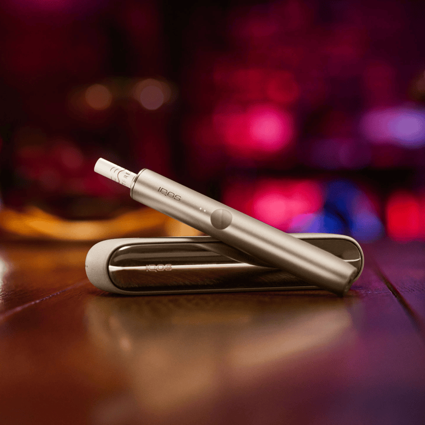 IQOS ILUMA Tabakerhitzer mit Stick im Holder vor einem farbigen Hintergrund