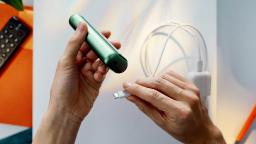Jemand schließt ein jadegrünes IQOS ILUMA PRIME Gerät an ein Ladegerät an