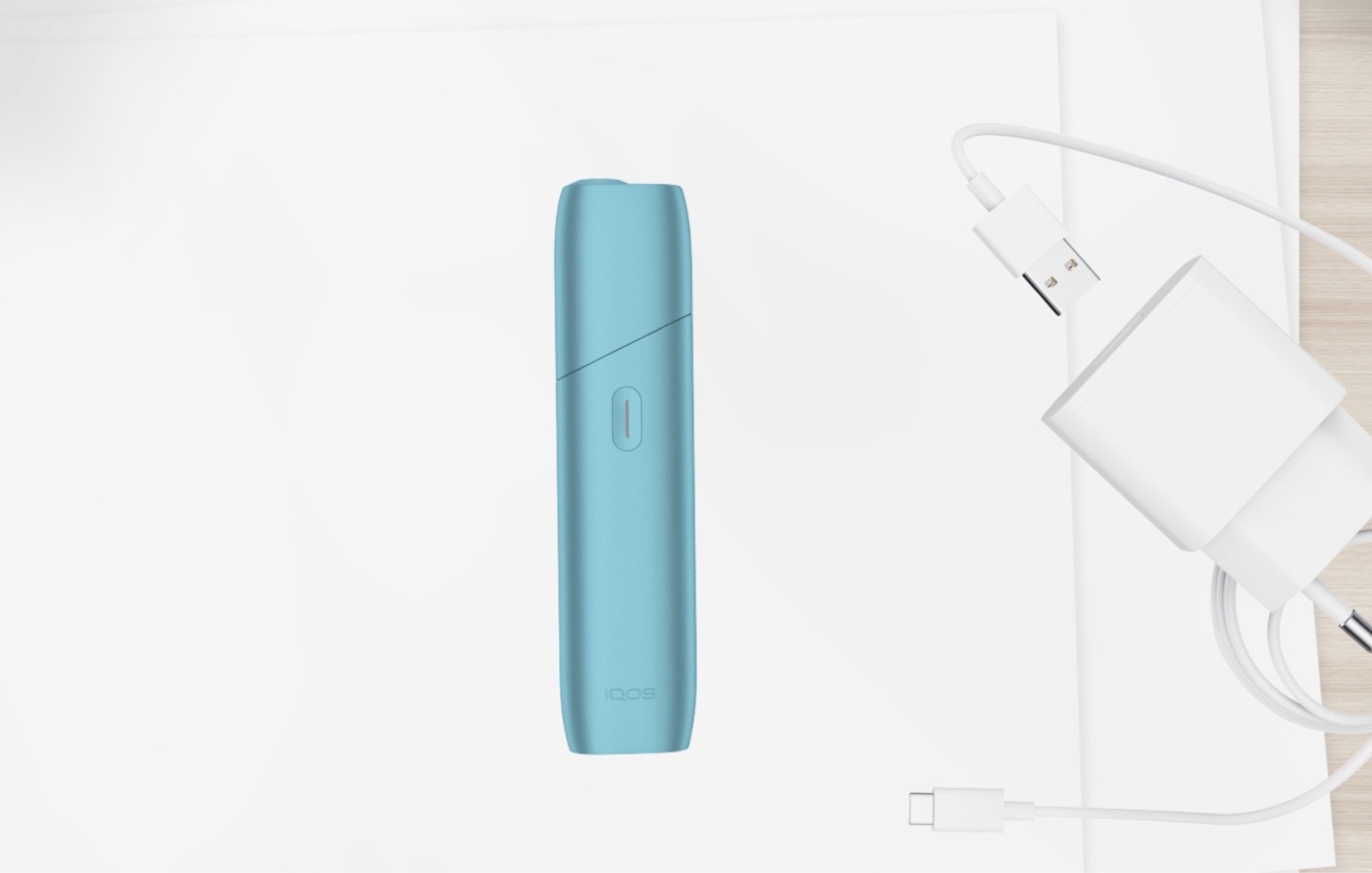 Türkiser IQOS ORIGINALS ONE liegt neben dem Aufladegerät