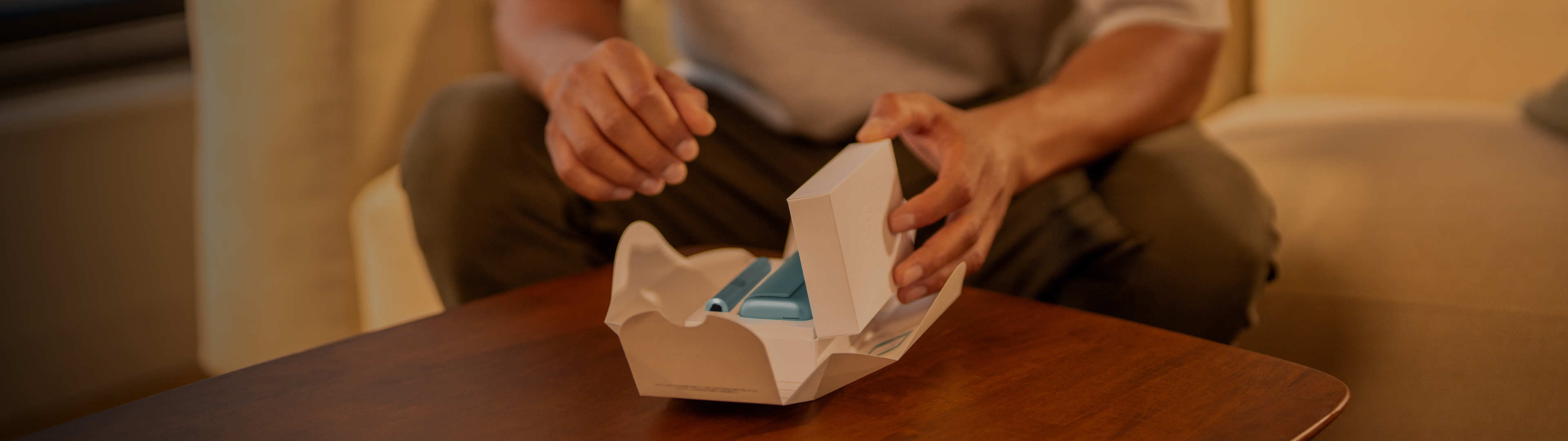 Eine Person öffnet eine Verpackung mit einem IQOS auf einem Tisch.