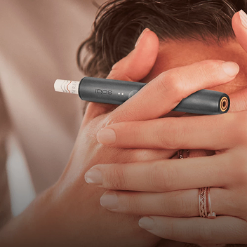 Person lächelt in die Kamera mit einem IQOS ILUMA im Fokus