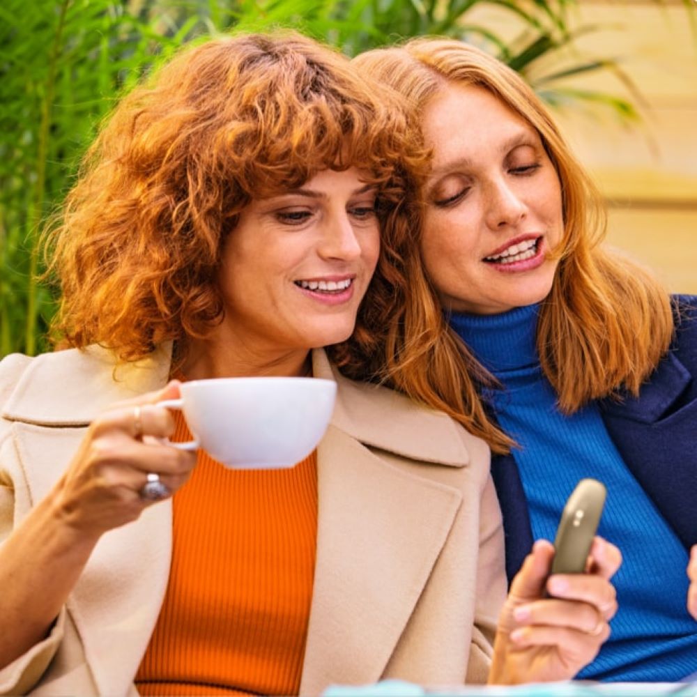 Black IQOS 3 device and mobile phone in two people's hands