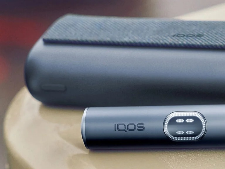 Hands holding smartphones and one IQOS device.