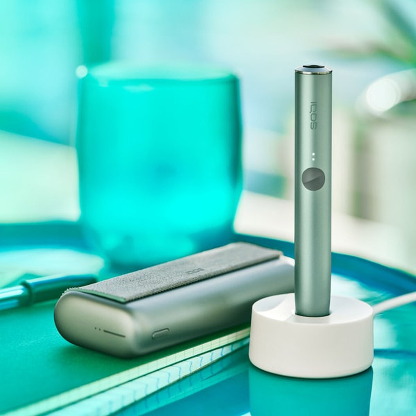 An IQOS ILUMA device in a charging station with a Pocket Charger on a table.