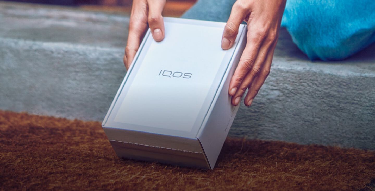 Two hands picking up a IQOS device box.