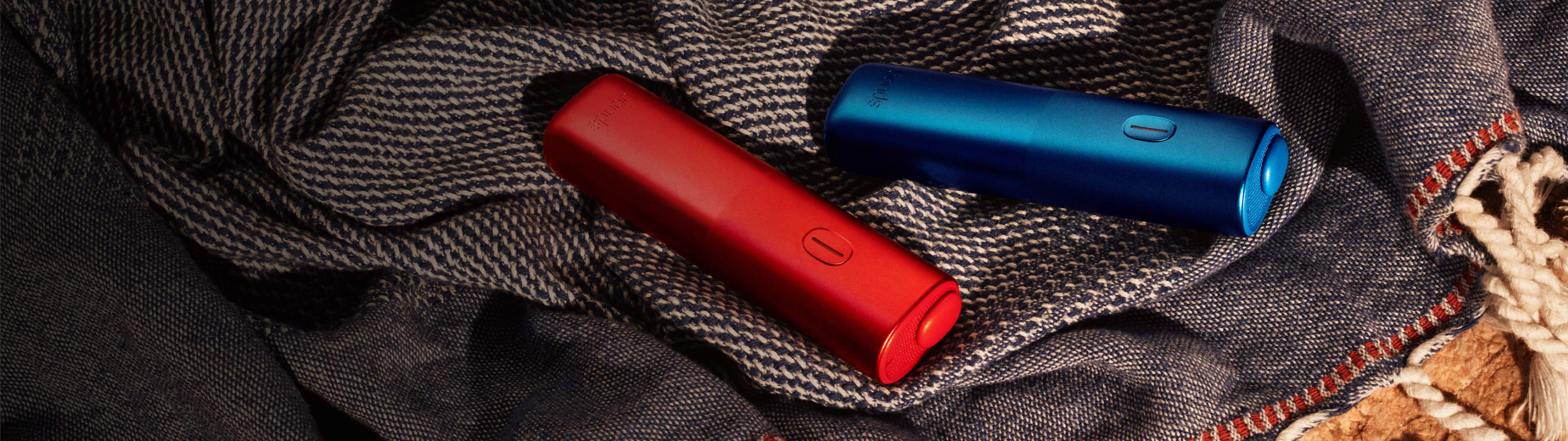 Appareils BONDS by IQOS rouge et bleu posés sur un tissu texturé foncé.