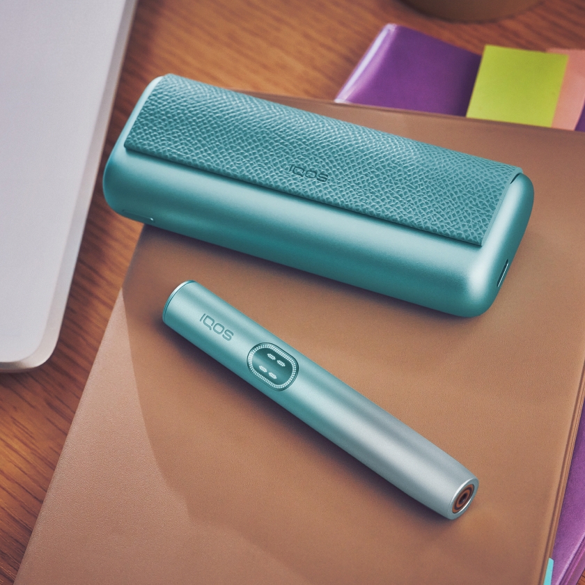 Appareil IQOS ILUMA i PRIME bleu et son chargeur sur un cahier marron