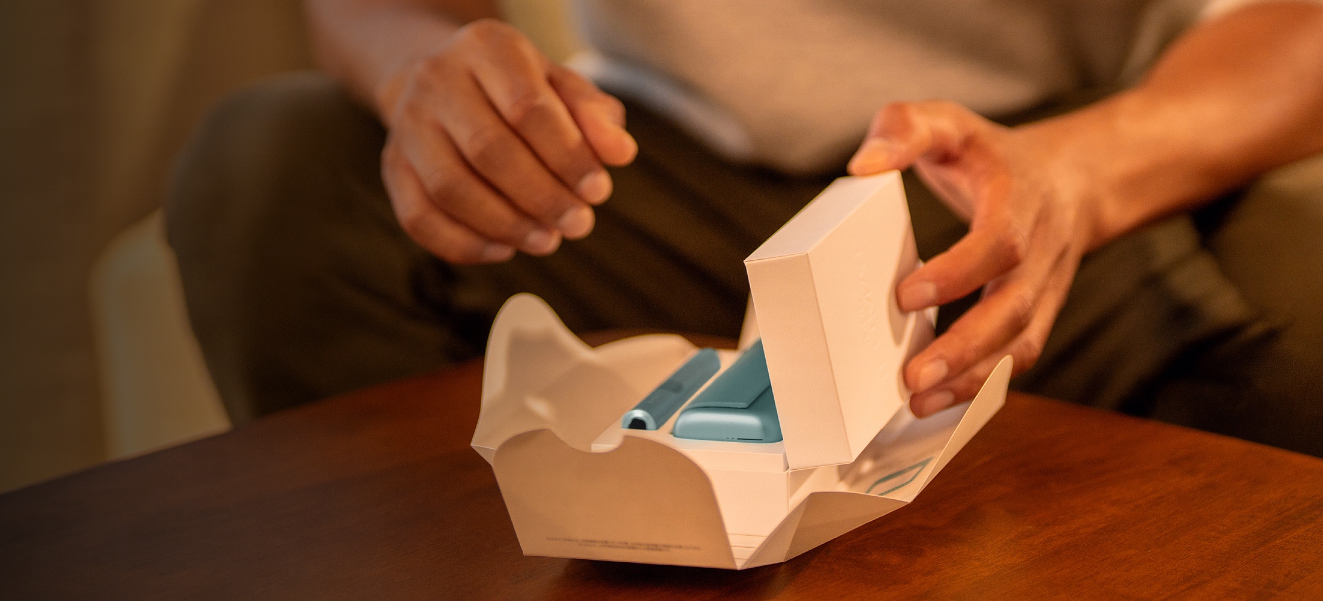 Une personne assise sur un canapé en train de déballer un appareil IQOS ILUMA bleu.