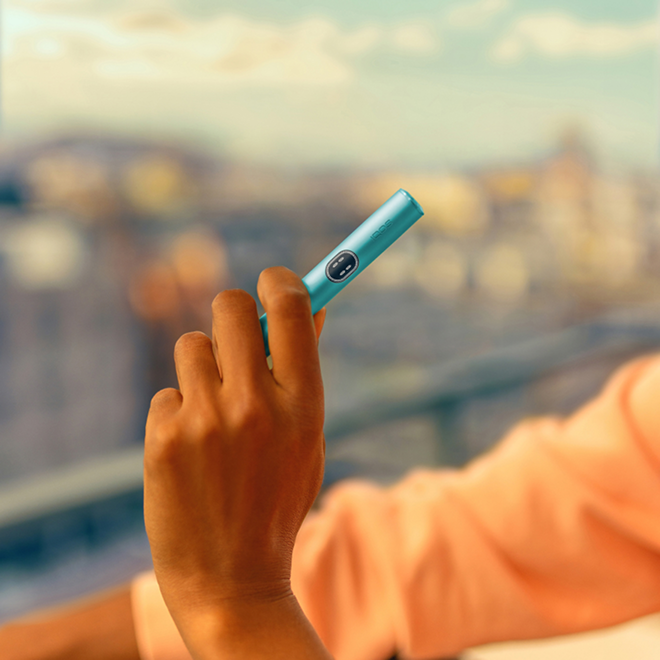Hand holding a Breeze Blue IQOS ILUMA i device in a city background