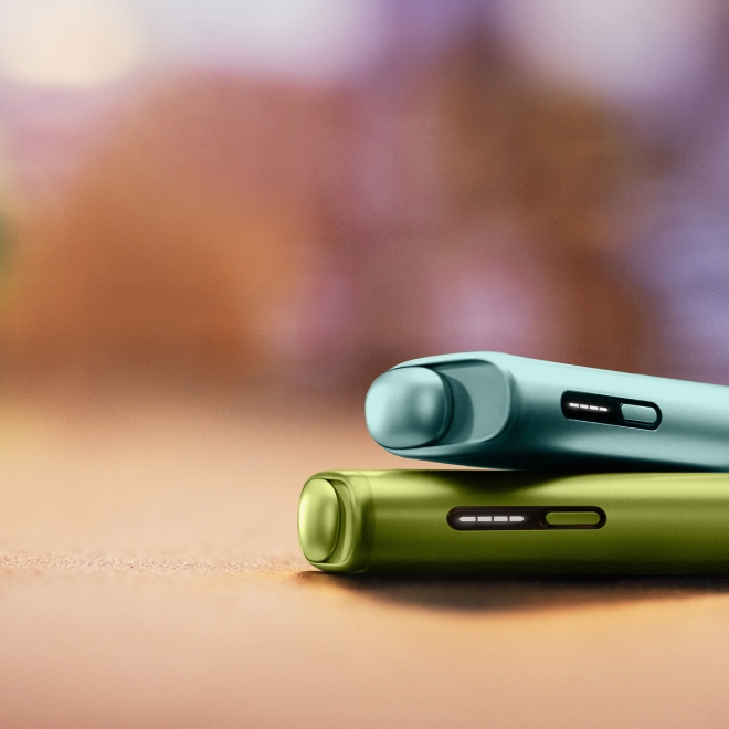A Breeze Blue IQOS ILUMA i ONE device on top of a Leaf Green IQOS ILUMA i ONE device.