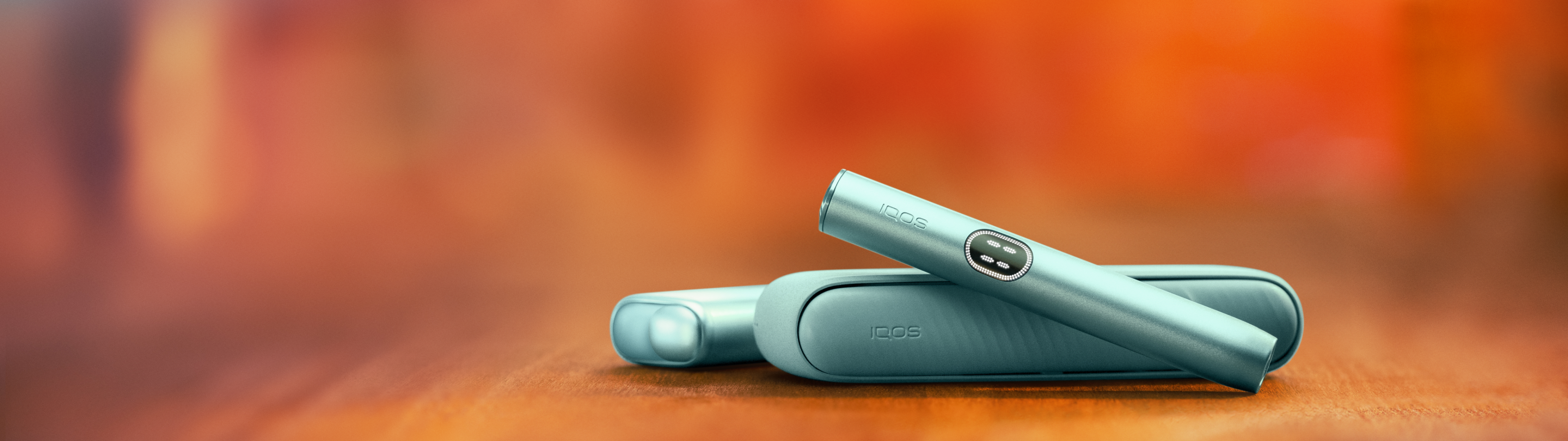 IQOS ILUMA i and IQOS ILUMA i ONE, οn an orange blurred background.