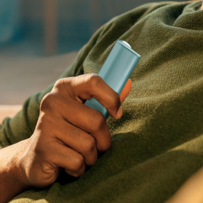Hand holding a breeze blue IQOS ILUMA i ONE device.