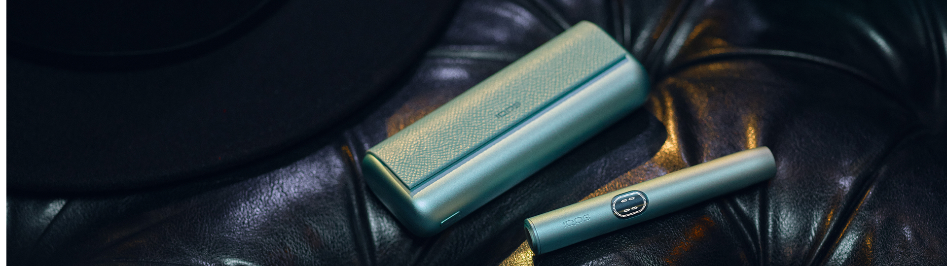 Primer plano de IQOS Iluma i verde metalizado sobre asiento de piel.