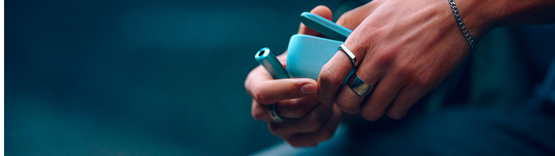 Primer plano de mano sosteniendo un IQOS Iluma i ONE azul al aire libre.