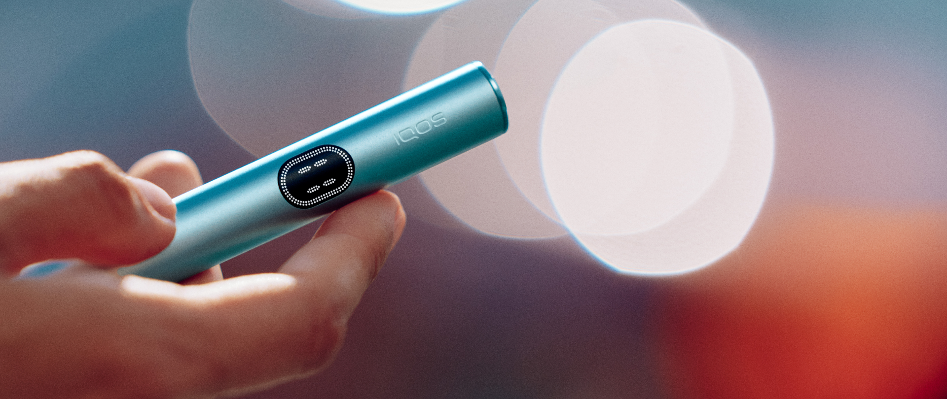 Persona sosteniendo dispositivo IQOS ILUMA-i color azul en ambiente nocturno borroso