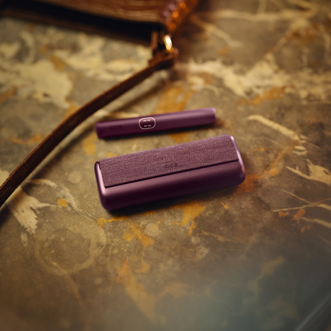 IQOS ILUMA PRIME color morado sobre mesa de madera, con luz cálida y detalles de textura en la superficie.