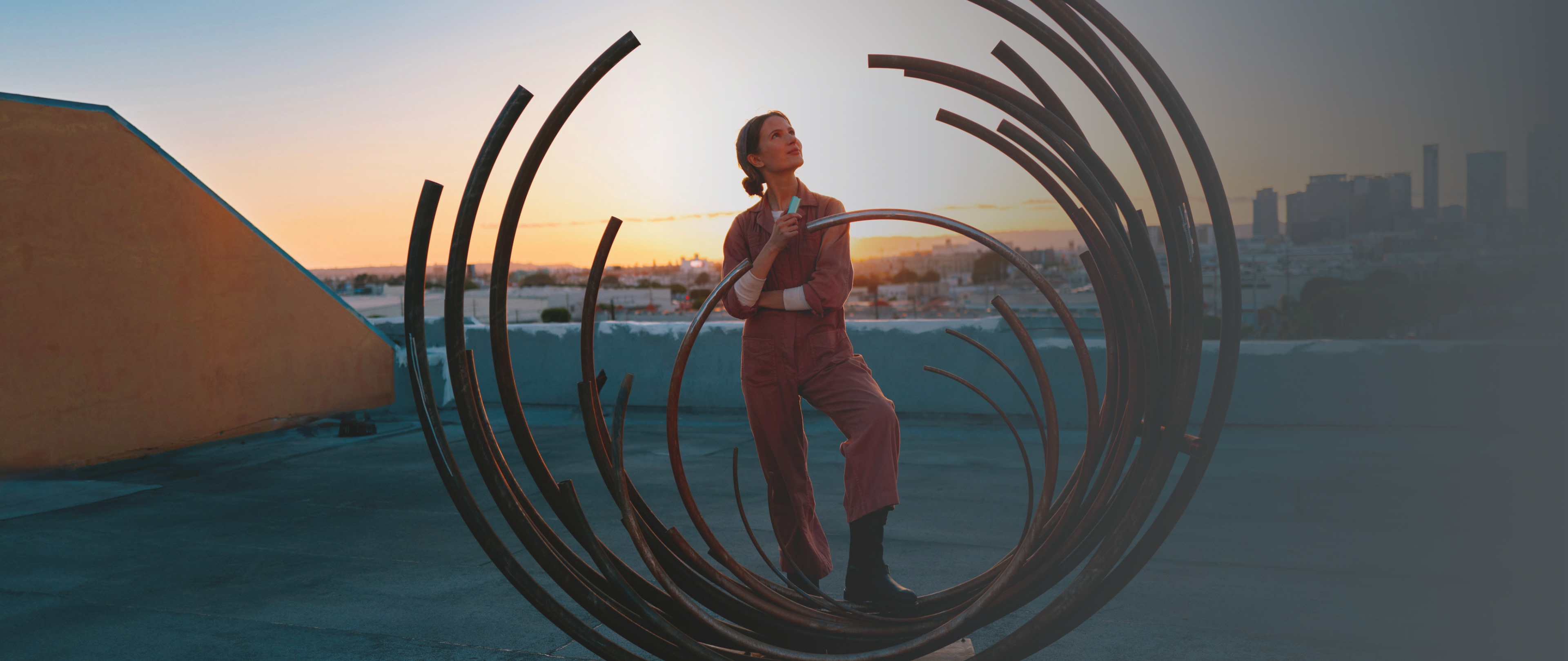 Mujer parada en estructura artística circular al aire libre, sosteniendo un dispositivo IQOS ILUMA i en mano y texto “Together Club”.