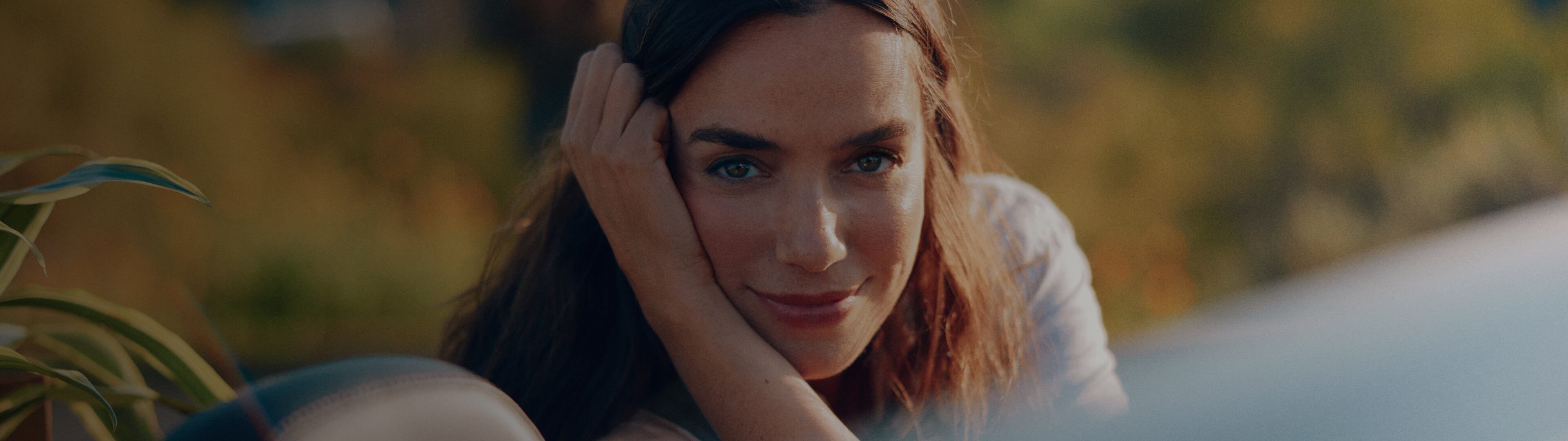 Mujer recargada sobre un auto descapotable en exterior, imagen panorámica con fondo natural.
