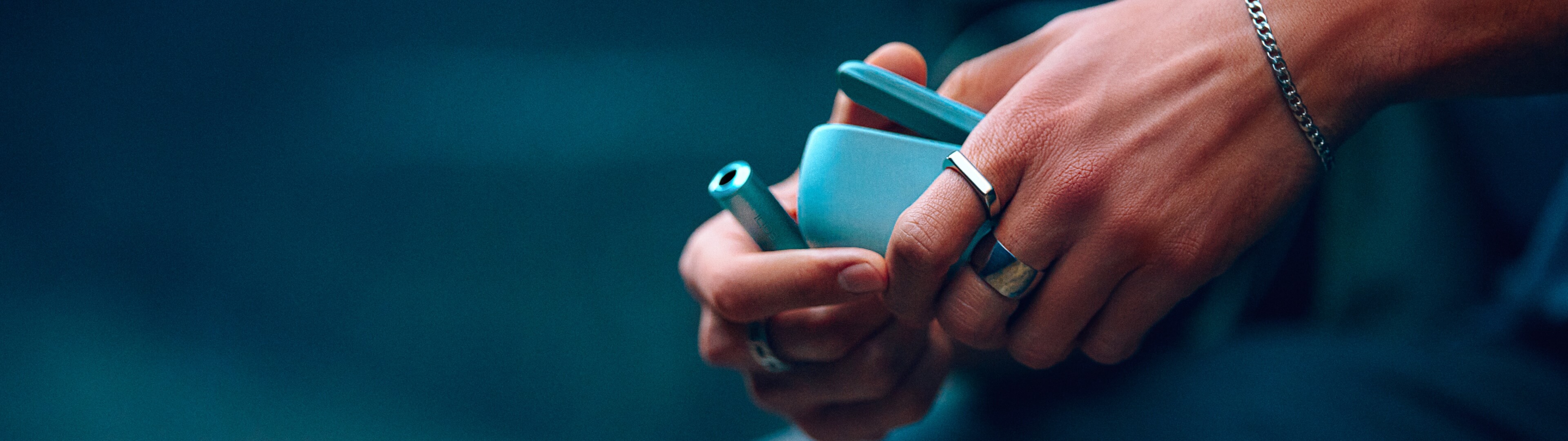 Manos sosteniendo un dispositivo IQOS ILUMA y una varilla, sobre fondo azul con texto promocional: “¿A dónde te llevará el camino libre de humo?”