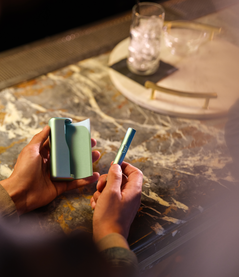 Dispositivo IQOS ILUMA verde, acompañado de texto: “95% menos sustancias nocivas comparado con cigarro”.