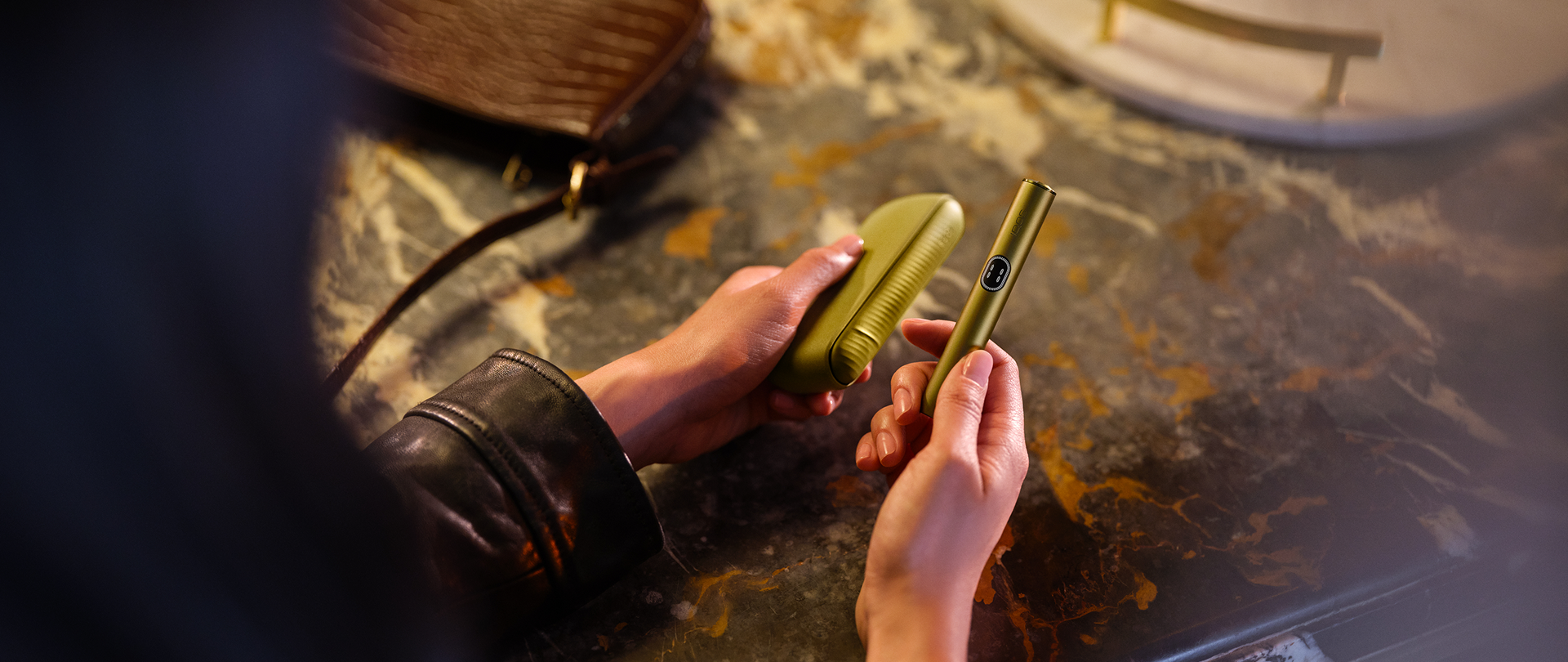 Persona sosteniendo IQOS Iluma i verde mientras lo enciende sobre una mesa con herramientas