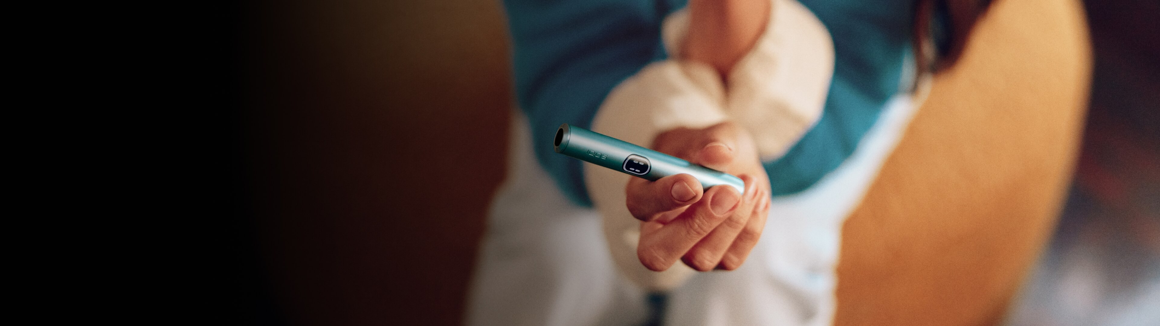Persona mostrando un IQOS ILUMA i One color turquesa desde arriba con fondo desenfocado.