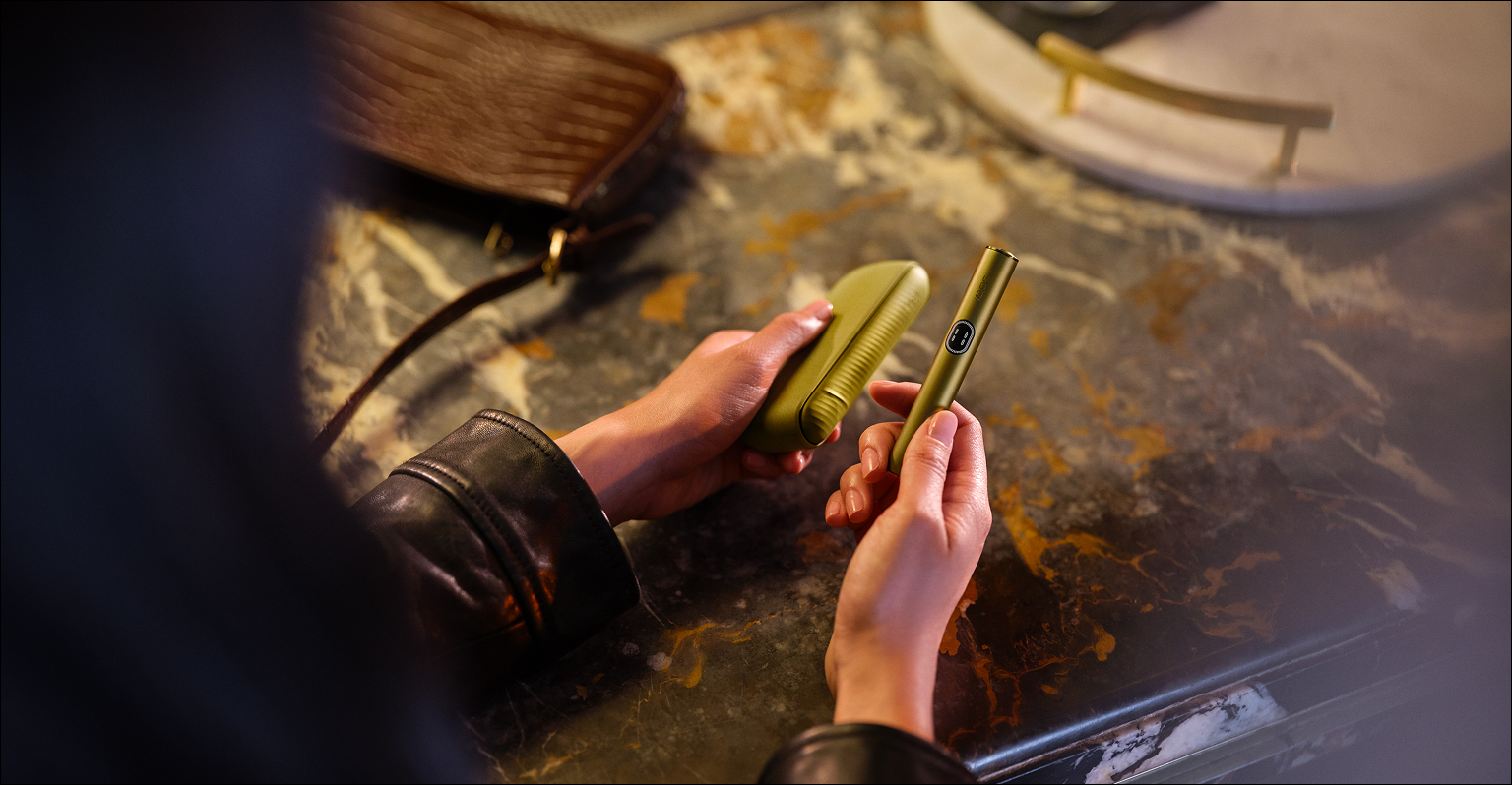 Persona manipulando un IQOS ILUMA i turquesa sobre una mesa con luz cálida.