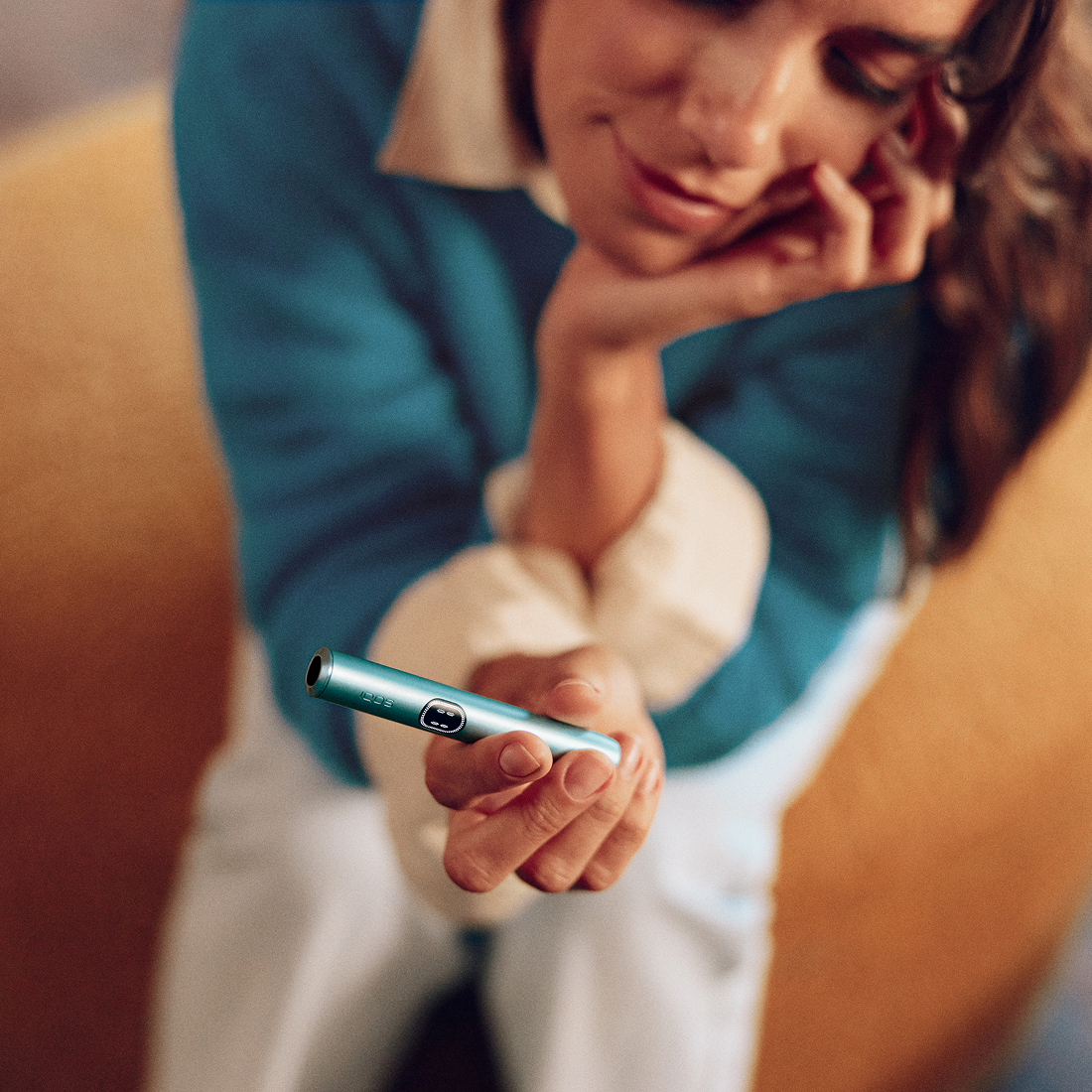 Mujer usando IQOS Iluma i turquesa recostada en sillón en ambiente cálido