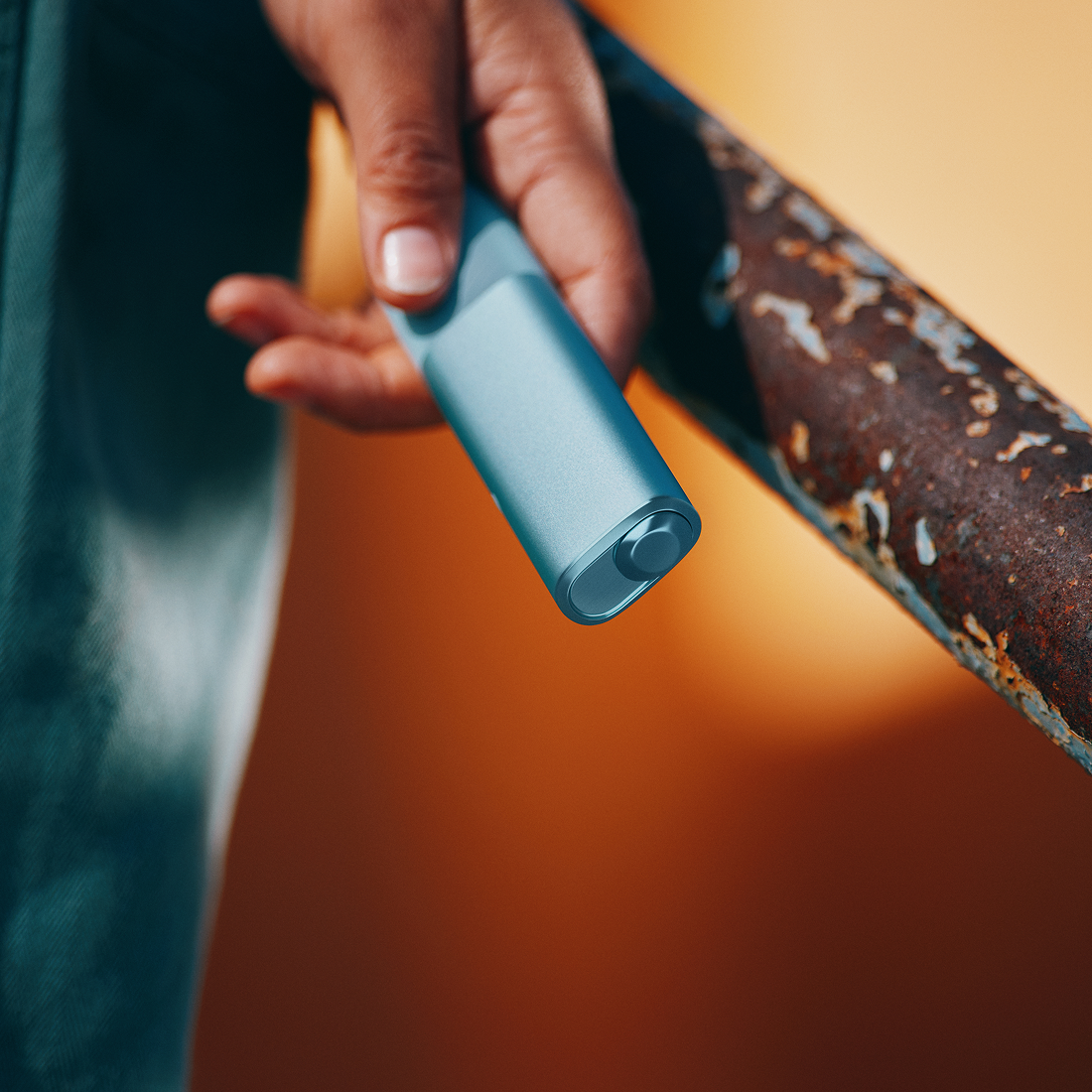 Persona usando IQOS Iluma i turquesa en exterior con barandal oxidado