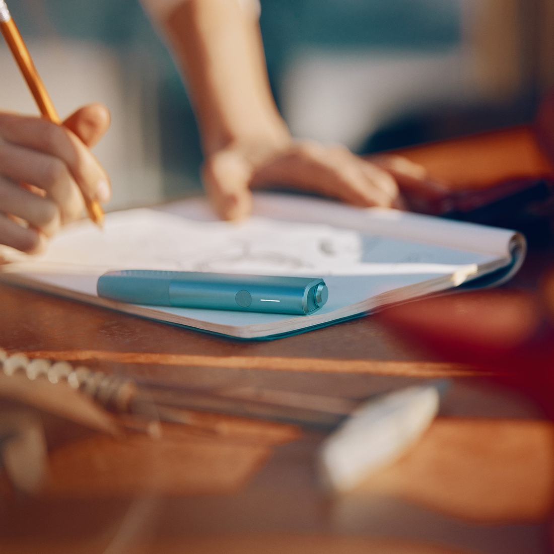 Persona tomando notas mientras usa IQOS Iluma i ONE turquesa sobre libreta