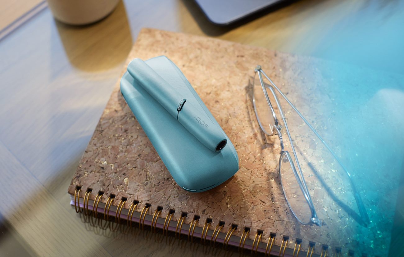 Laptop next to turquoise IQOS ORIGINALS DUO pocket charger.