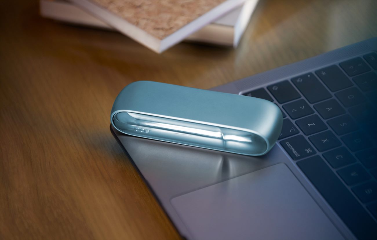 Laptop next to turquoise IQOS ORIGINALS DUO pocket charger.