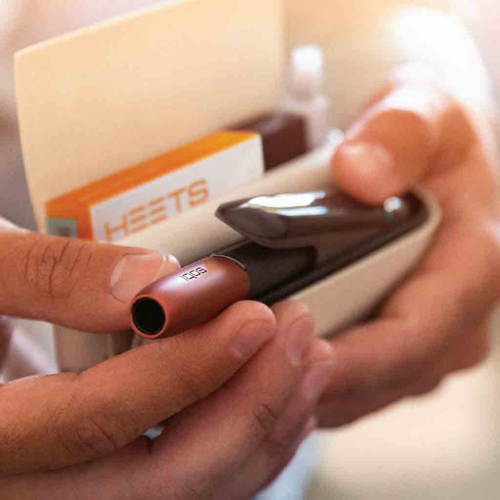 Woman holding a gold IQOS heated tobacco device